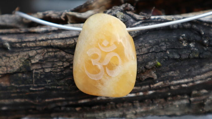 Ein Bernsteinanhänger mit einem eingravierten Om-Symbol hängt an einer Silberkette auf einem alten Holzstück.