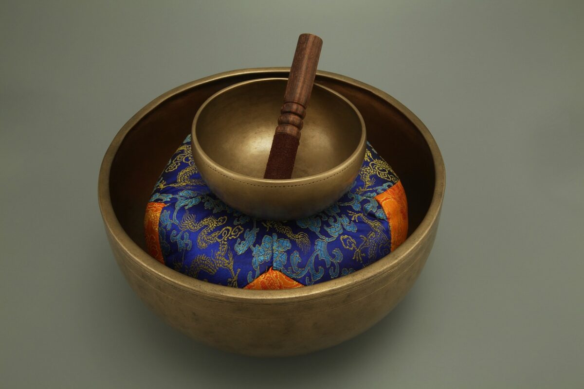 Eine tibetische Klangschale mit einem Klöppel liegt auf einem gemusterten Kissen.