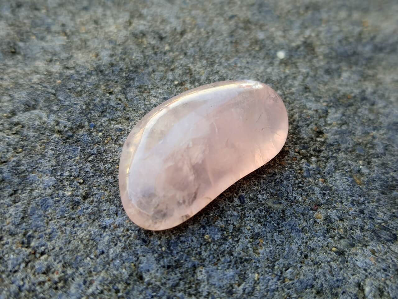 Ein rosa schimmernder Edelstein liegt auf einer rauen grauen Oberfläche.